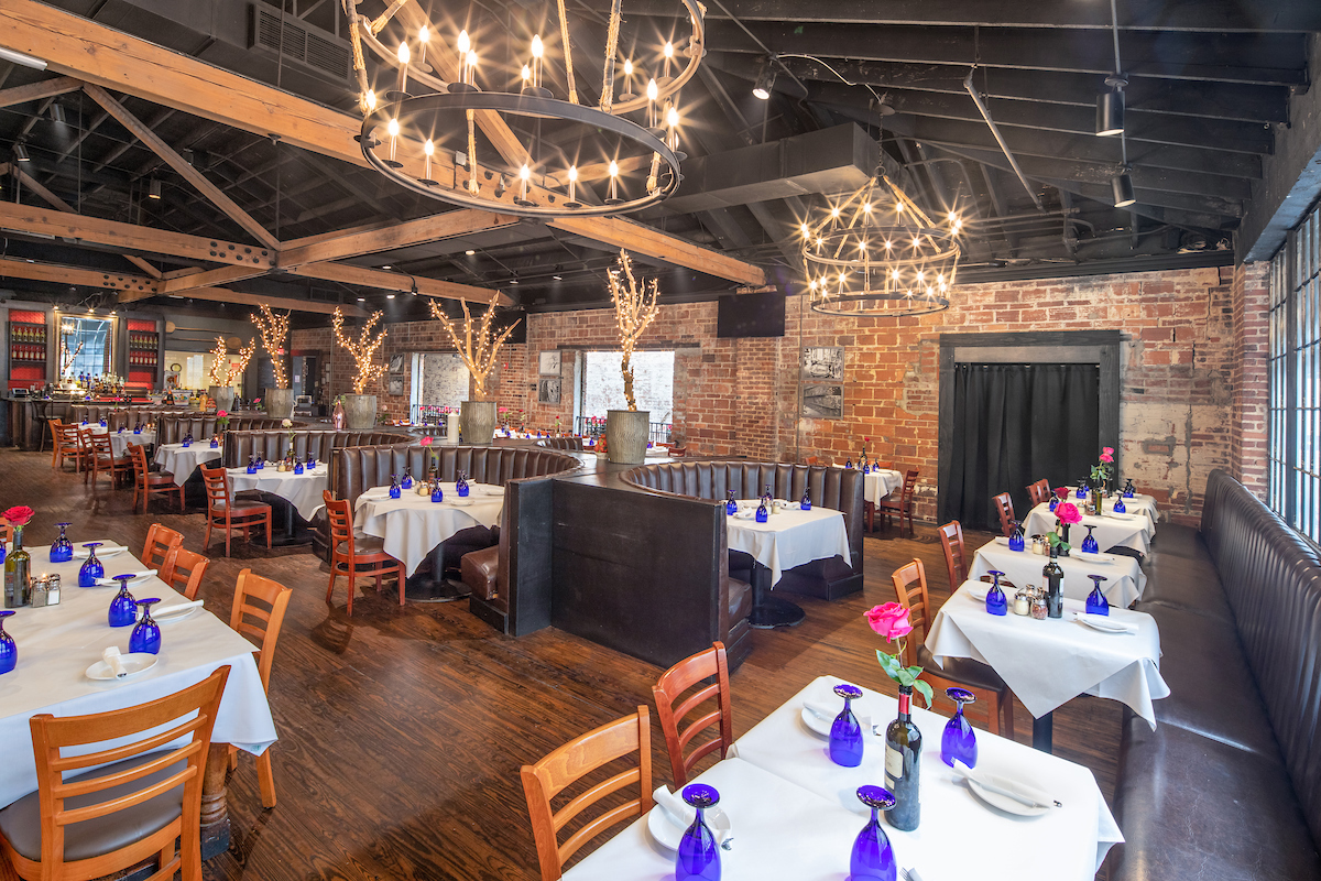 Amalfi dining room with chandeliers, exposed brick and tables set with blue glasses