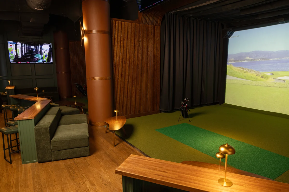 Green lounge seating, brass table lamps and a sports simulator at Peachtree Sporting Club