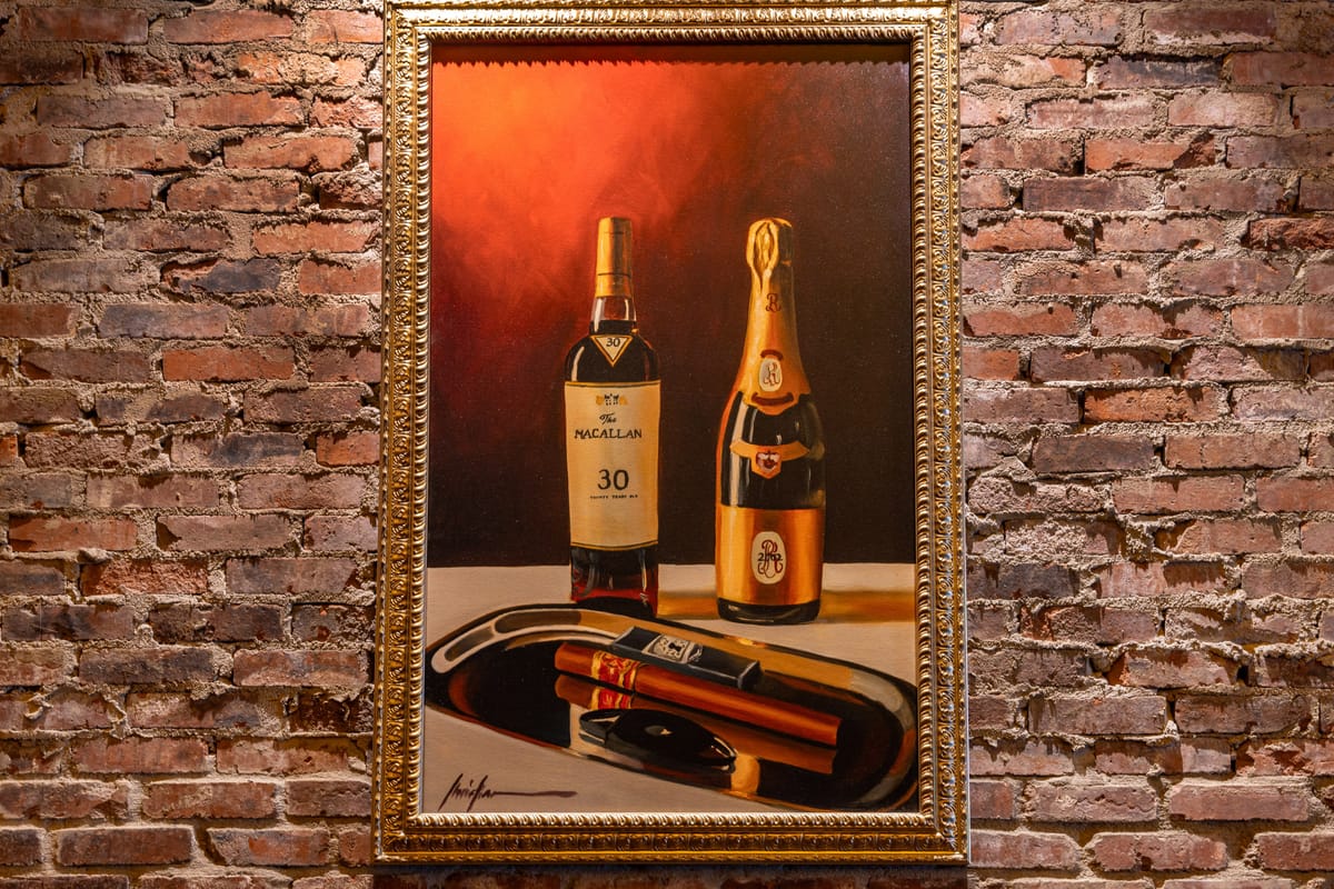 Framed spirits and cigar artwork on a brick wall at Red Phone Booth